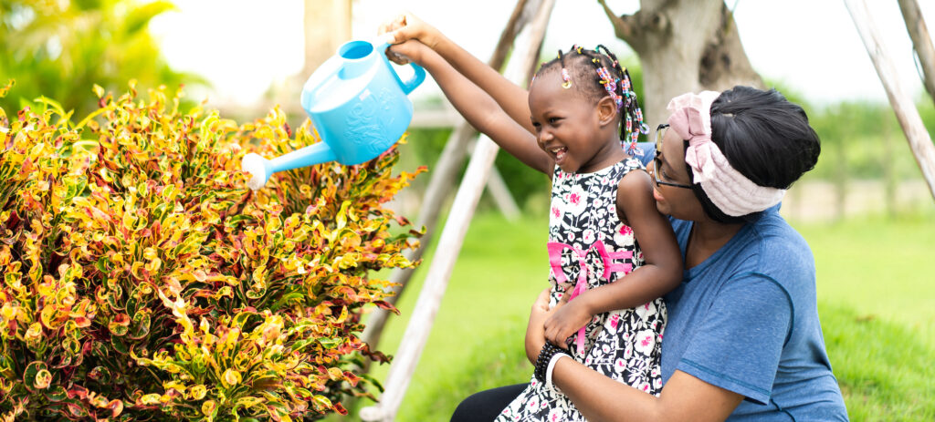 Black mother and daughter watering plants together